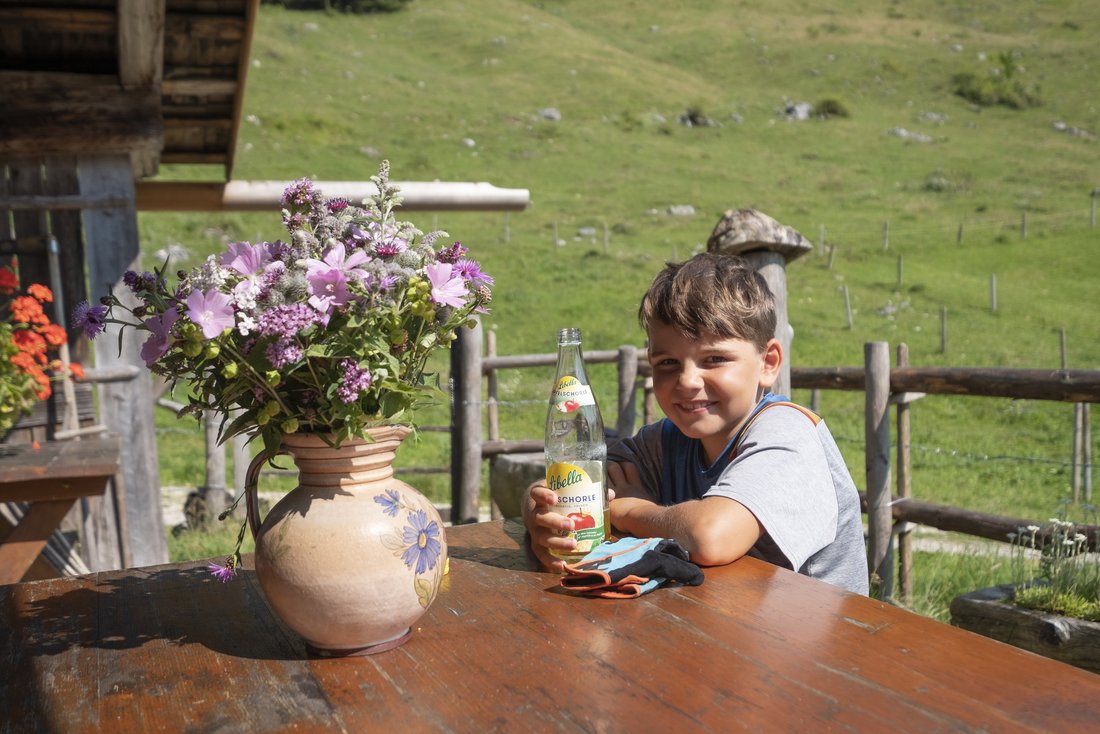 kleiner Junge trinkt eine Apfelschorle auf einer Almhütte in Schleching