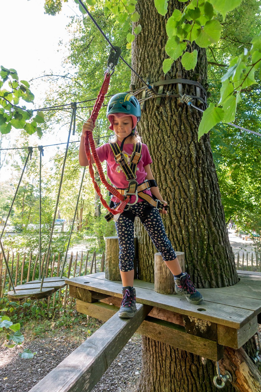Mädchen geht vorsichtig und mit Klettergurt gesichert über einen Holzbalken im Hochseilgarten Übersee