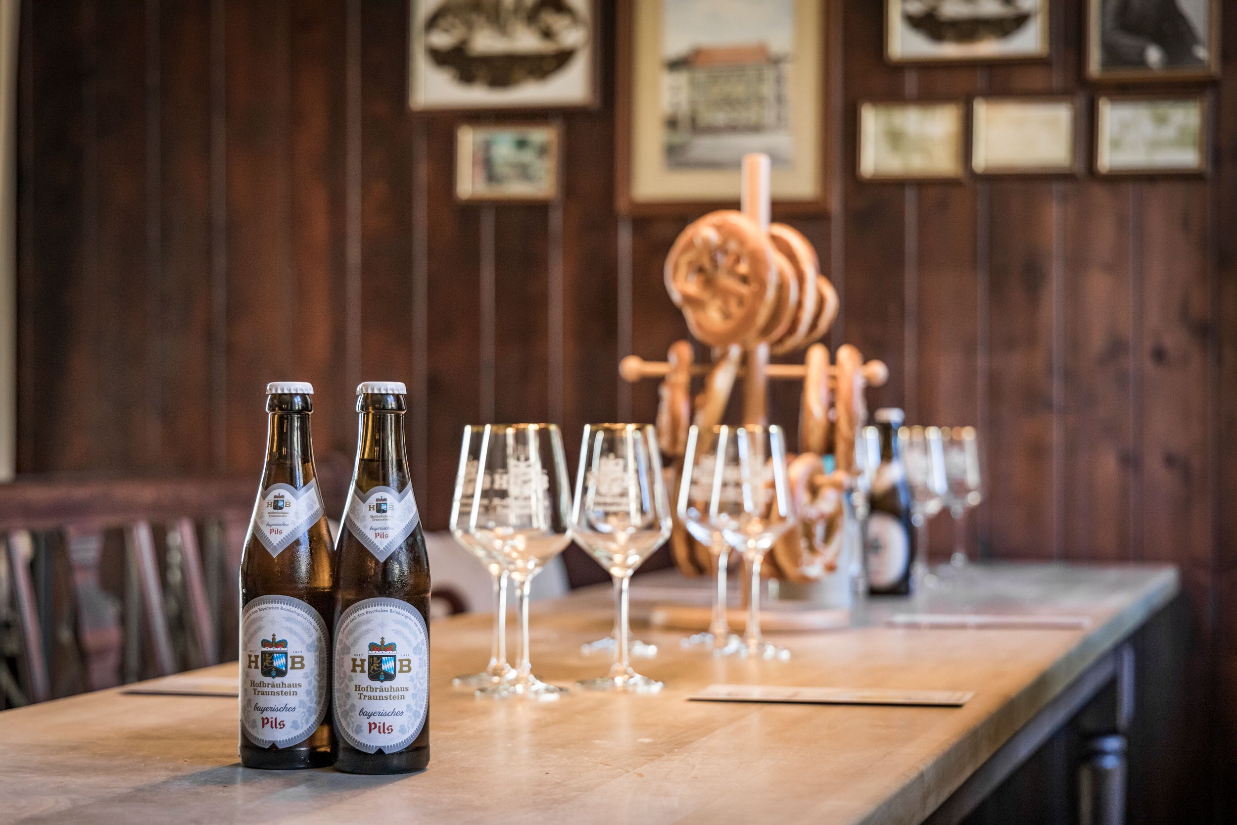 Zwei Flaschen Bayerisches Pils vom Hofbräuhaus Traunstein auf dem Tisch, vor Gläsern und Laugenbrezen