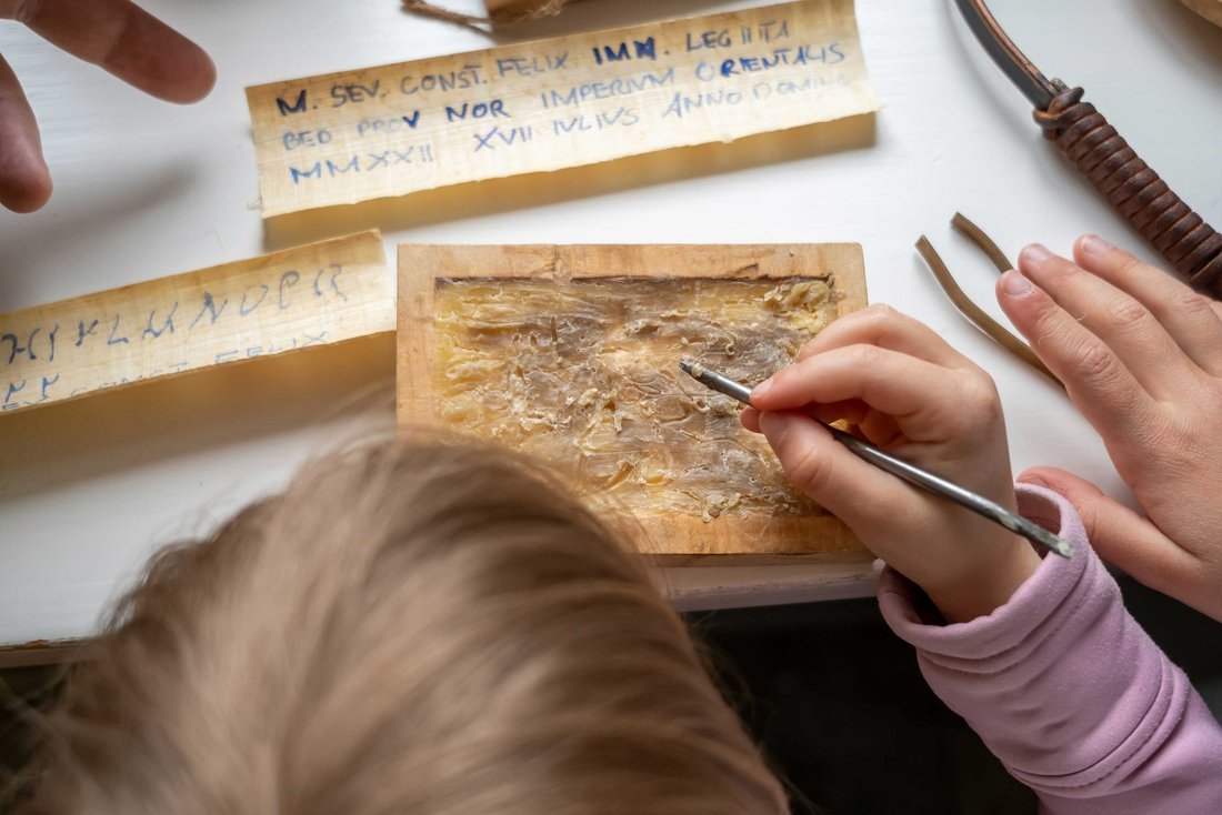 Kind schreibt mit einer Griffel in eine Wachstafel