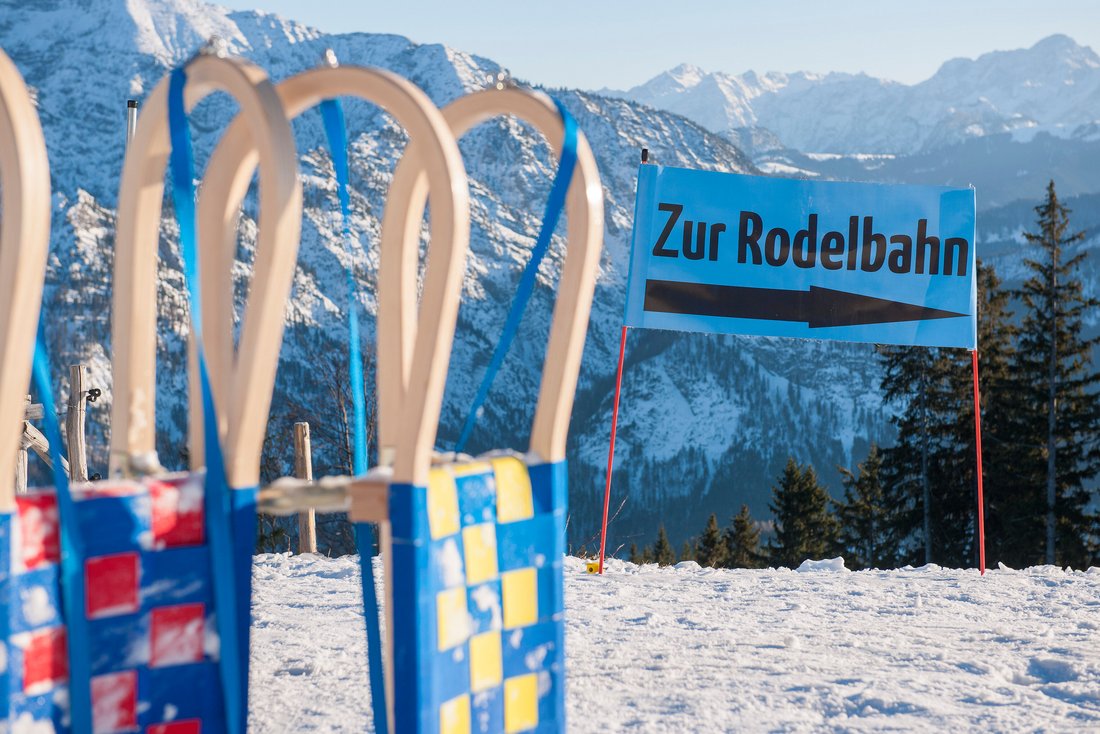 Zwei Rodeln vor dem Banner mit Aufschrift "Zur Rodelbahn" auf dem Unternberg