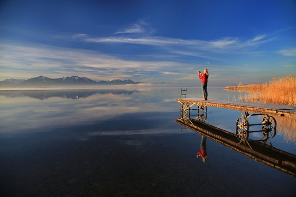 The photographer stands at the end of the footbridge from the Chiemsee and takes photos in the Chiemgau Alps