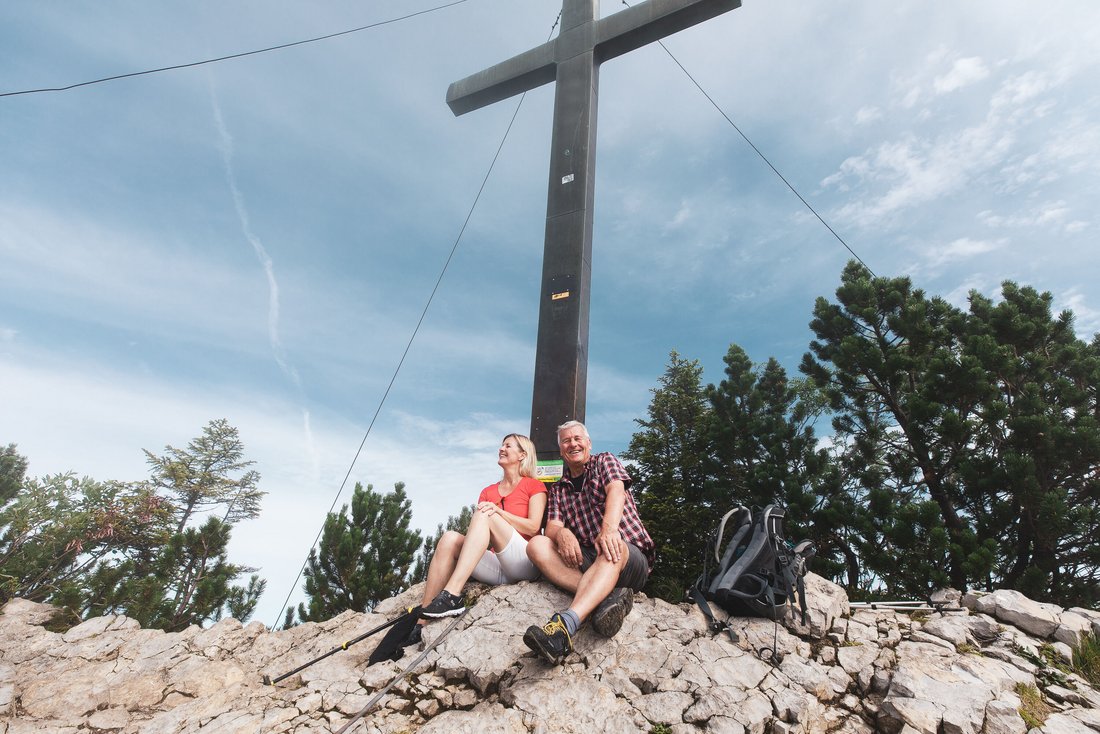 Wanderpaar sitzt vor dem Dürnbachhorn Gipfelkreuz