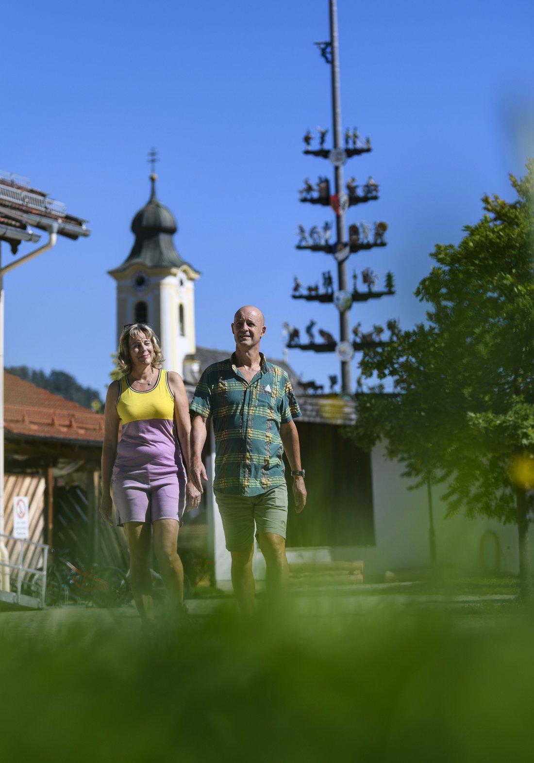 Pärchen spaziert am Dorfplatz der Gemeinde Schleching mit der katholischen Kirche im Hintergrund