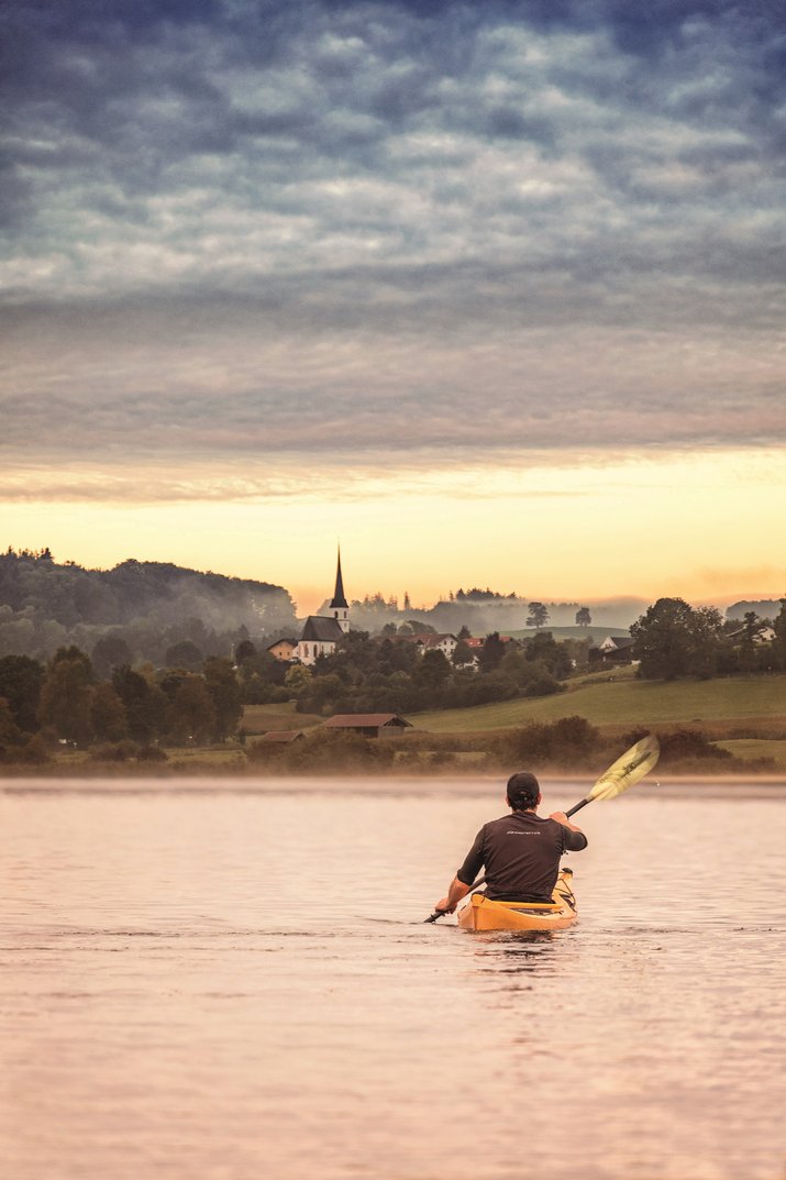 Kayakers at sunset on the Tachinger See with a view of the town of Taching am See