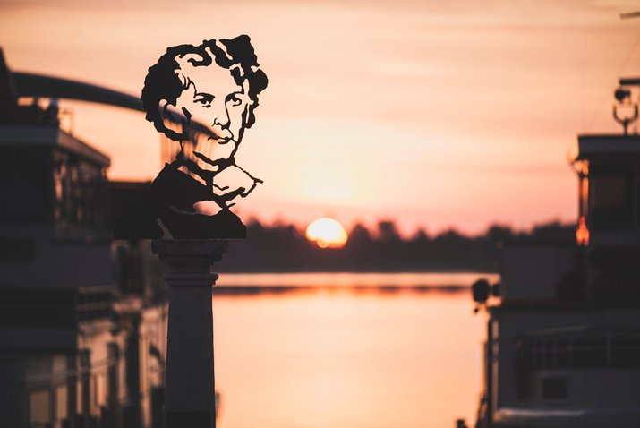Der Sonnenaufgang am Hafen in Prien scheint durch die König Ludwig Statue