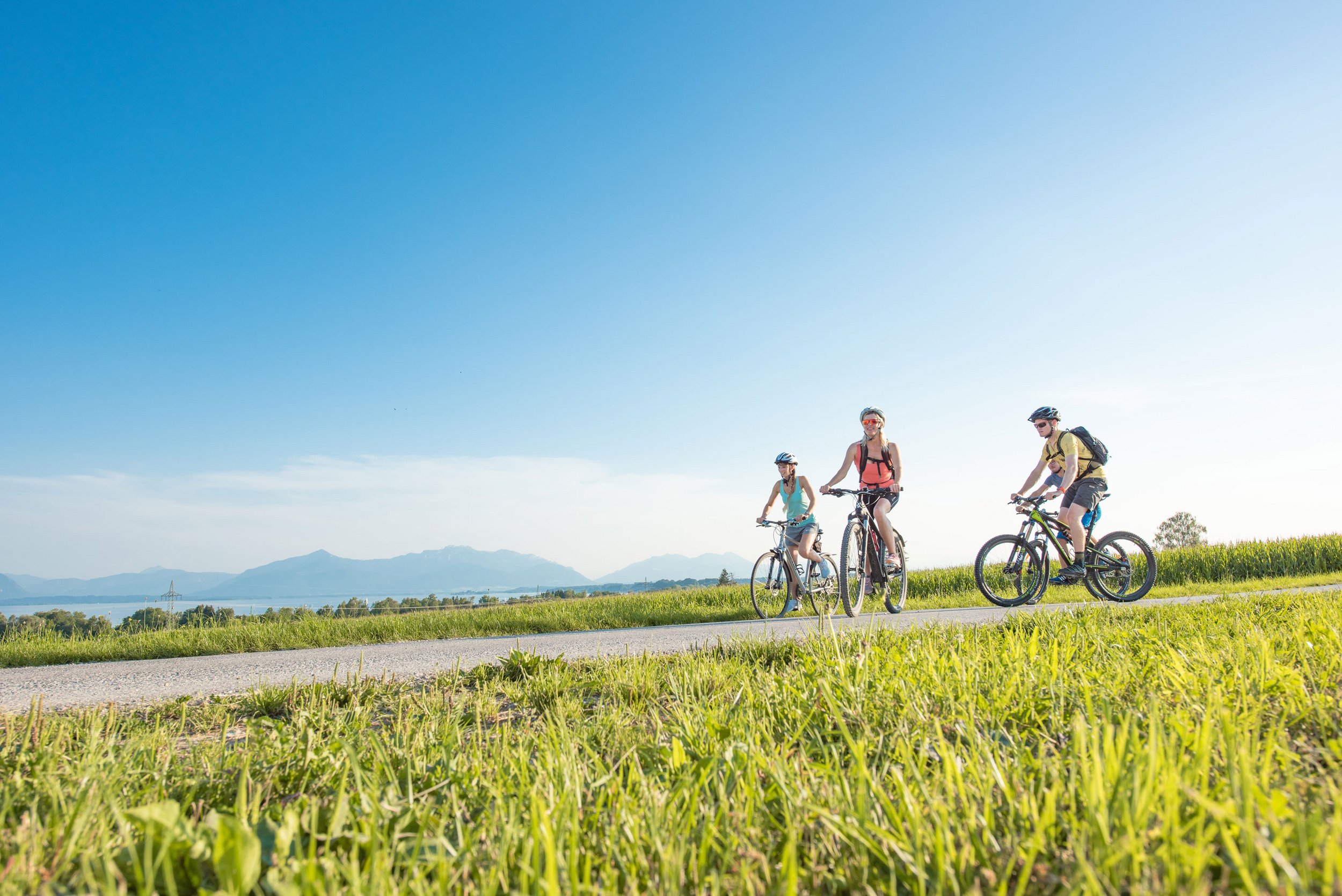 Eine Fahrradgruppe ist im Frühling bei Seebruck am Chiemsee im Chiemgau unterwegs. Im Hintergrund sind die Chiemgauer Berge sichtbar
