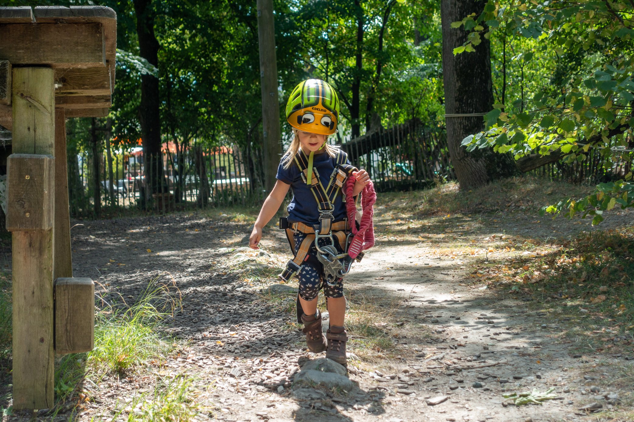 Mädchen geht mit Helm und Klettergurt ausgestattet zum Einstieg des Kinderparcours.