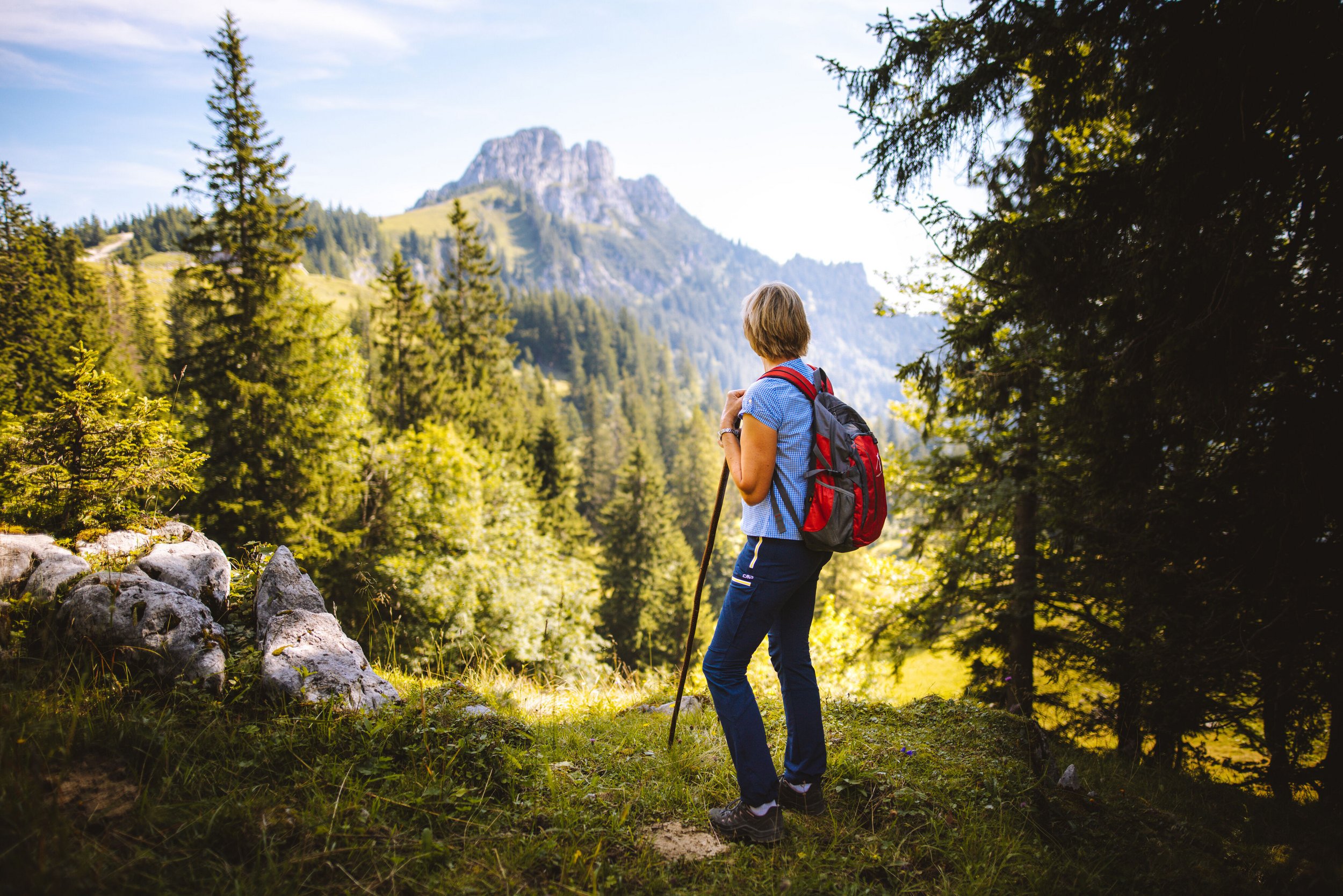 Eine Kräuterwanderführerin im Wald im Hintergrund der Blick auf die Kampenwand im Chiemgau