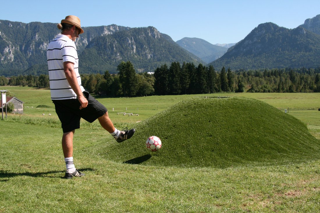 Junge beim Abschuss des Fußballs auf dem Soccer Golf Park in Inzell mit den bayerischen Alpen im Hintergrund