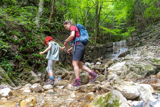 Mutter und Tochter überqueren kleinen Bach beim Wandern im Wald 