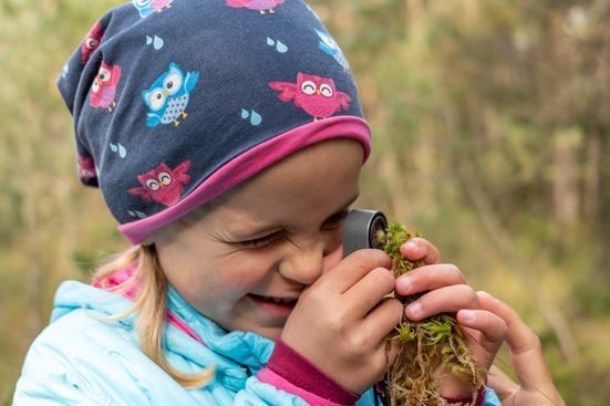 Mädchen schaut durch eine Lupe ein Moos im Schönramer Filz an