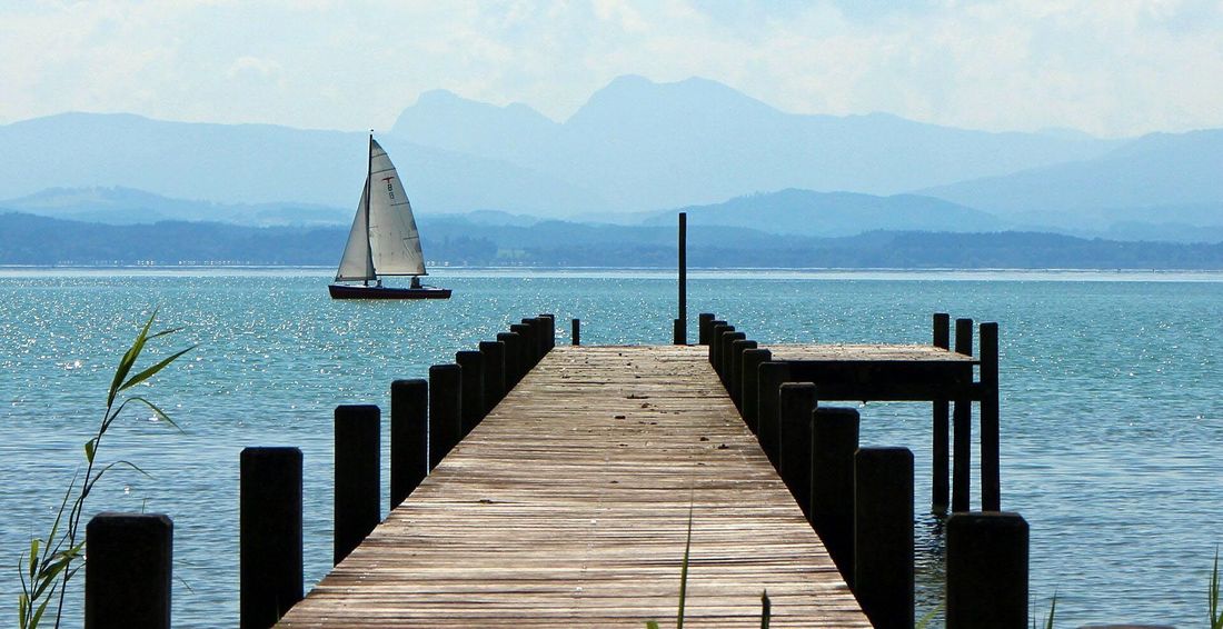 Blick über den Chiemsee mit Segelboot und den Bayerischen Alpen im Hintergrund.