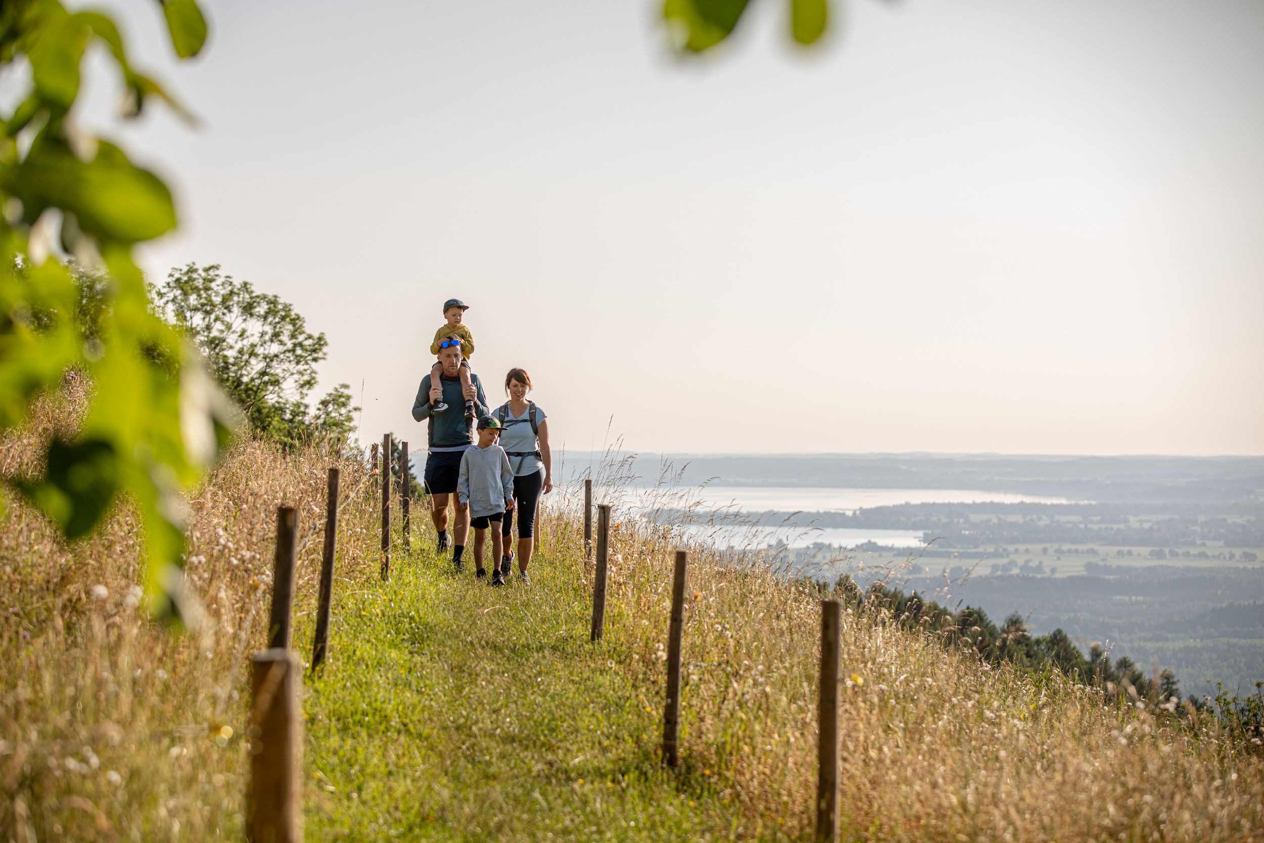 Familie wandert im Sommer bei den Grassauer Almen, im Hintergrunf schimmert der Chiemsee