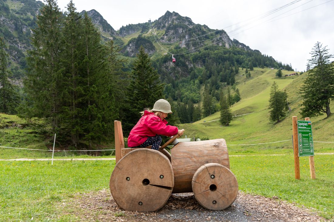 Mädchen sitzt auf einem großen Traktor aus Holz auf dem Spielplatz der Mittelstation des Hochfelln